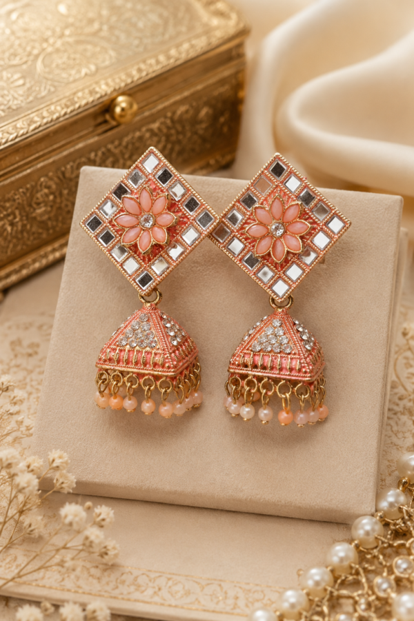 Close-up of designer peach floral jhumka earrings with mirror work, crystal detailing and pearl bead tassels.